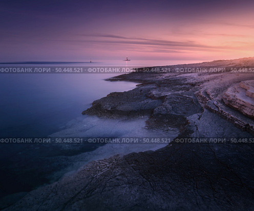 Rocky sea coast and lighthouse at colorful sunset in summer. Beautiful landscape with beach, stones in blurred blue water, purple sky at dusk. Nature. Adriatic sea at night, Kamenjak, Croatia. Travel. Стоковое фото, агентство Ingram Publishing / Фотобанк Лори