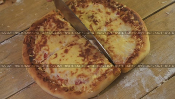 Round pizza is divided with a knife into several equal parts on a wooden table. homemade Italian cuisine. Стоковое видео, видеограф Strunov David / Фотобанк Лори