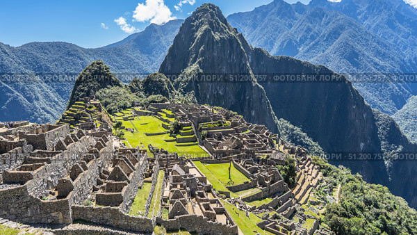 Ruins of the famous Lost City of the Incas Machu Picchu. Stone walls, dilapidated buildings, terraces with green grass. Huayna Picchu and a mountain range against a blue sky and clouds. Peru. Cusco. Стоковое фото, фотограф Вера Ивановна Кубарева / Фотобанк Лори