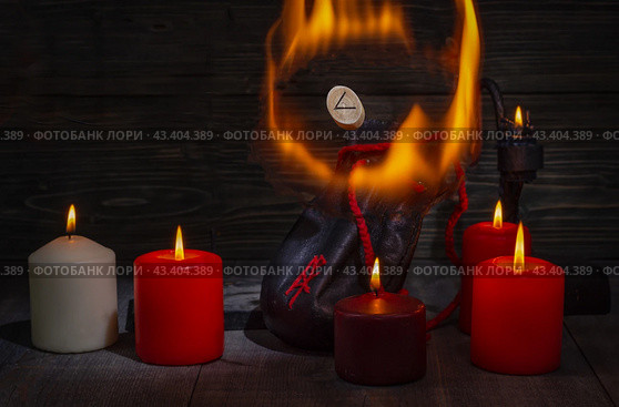 Rune Kenaz surrounded by flames. A composition of burning candles, an old leather bag for Scandinavian runes with a bokeh effect. Стоковое фото, фотограф Анищенко Геннадий / Фотобанк Лори