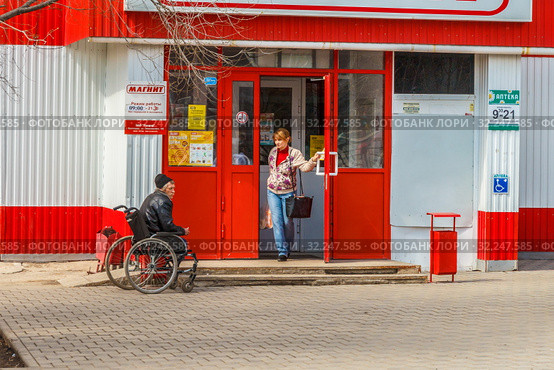 Russia, Samara, April 22, 2016: a sick man in a wheelchair asks for alms near the store, the text in Russian: a pharmacy. Редакционное фото, фотограф Акиньшин Владимир / Фотобанк Лори