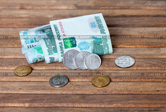 Russian rubles. Several ruble coins of different denominations and 1000 ruble paper banknotes rolled up on wooden background. Concept of Russian economy, foreign investment, business, banking system and inflation. Стоковое фото, фотограф Виктория Катьянова / Фотобанк Лори