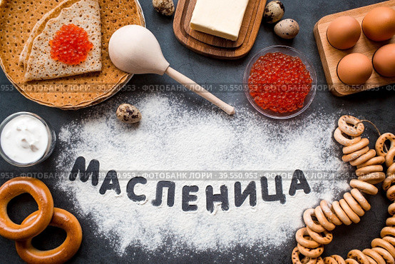 Русские традиции. Русский праздник Масленица. Стопка блинчиков, красная икра, бублики, рогалики, баранки, деревянная ложка, яйца и сливочное масло. Русская надпись "Масленица" написана мукой. Вид сверху. Стоковое фото, фотограф Photojuli / Фотобанк Лори