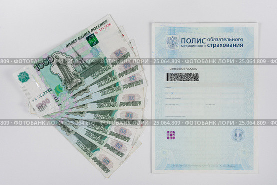 Рядом с медицинским полисом лежит пачка веером тысячерублевых купюр, белый фон. Стоковое фото, фотограф Иванов Алексей / Фотобанк Лори