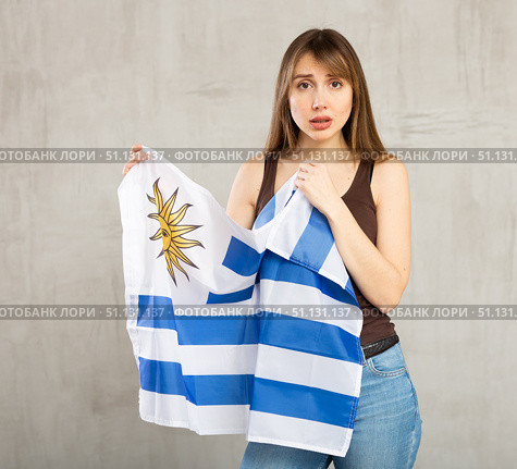 Sad young woman holding flag of Uruguay against unicoloured background. Стоковое фото, фотограф Яков Филимонов / Фотобанк Лори