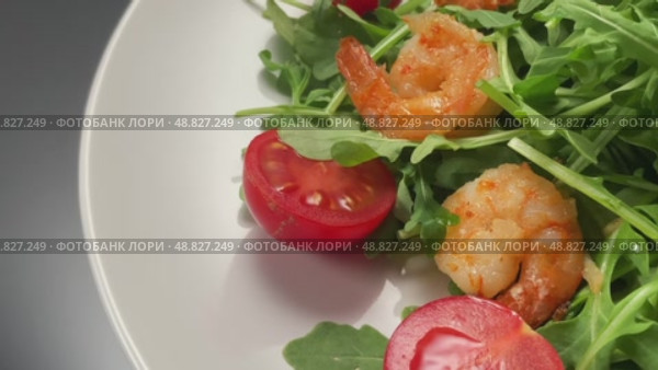 Салат из руккола с тигровыми креветками и помидорами черри на белой тарелке. Вид сверху, крупным планом. Стоковое видео, видеограф Максим Коломыченко / Фотобанк Лори