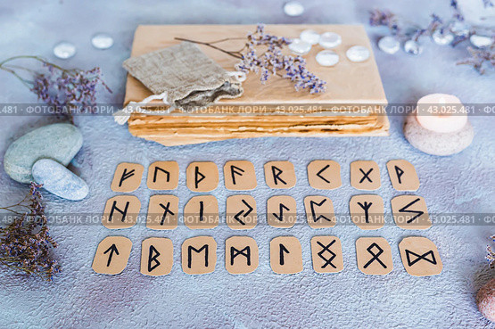 Scandinavian runes for fortune telling are  in three rows, a book, stones and a candle on the table. Стоковое фото, фотограф Елена Руй / Фотобанк Лори