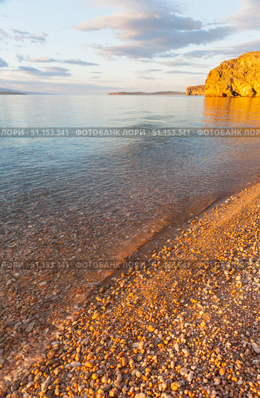 Scenic sunset landscape of Baikal Lake. View of clear transparent water on pebble beach of Small Sea and rocky coast of Olkhon Island on quiet August evening. Picturesque seascape. Natural background. Стоковое фото, фотограф Виктория Катьянова / Фотобанк Лори