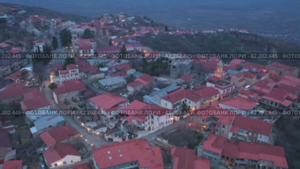 Scenic view from drone of Signagi township with narrow winding streets and brownish roofs on steep hill in foothills of Gombori Range in spring twilight, Georgia. Стоковое видео, видеограф Яков Филимонов / Фотобанк Лори