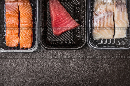 Selection of raw colorful fish fillets : salmon, tuna and codfish in plastic boxes on dark rustic background, top view, border, place for text. Healthy Seafood concept. Стоковое фото, агентство Ingram Publishing / Фотобанк Лори