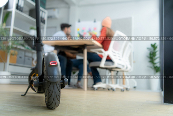 Selective focus of electric scooter in modern office with group meeting blurred background. Стоковое фото, агентство Ingram Publishing / Фотобанк Лори