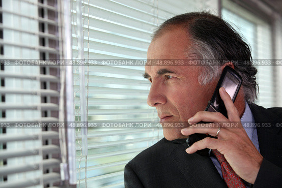 Senior businessman looking through blinds whilst making call. Стоковое фото, агентство Ingram Publishing / Фотобанк Лори