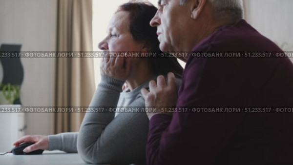 Senior couple using laptop together in the room. Embracing elderly man and woman reading email or online shopping choice. Old man and woman talk at table in home together on internet, social media. 4K. Стоковое видео, видеограф Марина Демидюк / Фотобанк Лори