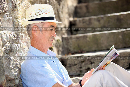 Senior man reading a magazine on some old stone steps. Стоковое фото, агентство Ingram Publishing / Фотобанк Лори