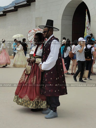 Seoul - June 21, 2017. Black couple in Korean traditional costumes in front of the Gates of Gyeongbokgung Palace. Пара афроамериканцев в корейских национальных костюмах. Редакционное фото, фотограф Александр Кузнецов / Фотобанк Лори