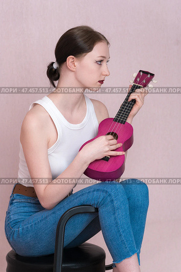 Serious young female musician playing ukulele, sitting on bar stool and looking away. Стоковое фото, фотограф А. А. Пирагис / Фотобанк Лори