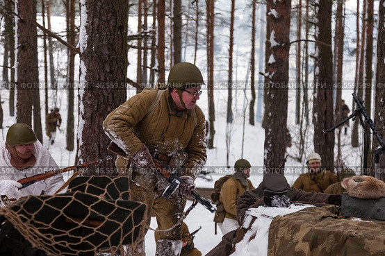 Sestroretsk, Russia - February 19, 2023: Snow-covered landscape sets the stage for a group of soldiers engaged in a reenactment of a historic winter battle. Редакционное фото, фотограф Aleksandr Golubev / Фотобанк Лори