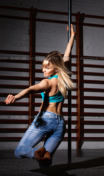 Sexy young woman in ripped jeans practicing pole dancing in dark fitness studio. Стоковое фото, фотограф Яков Филимонов / Фотобанк Лори