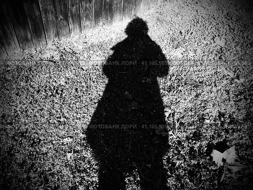Shadow of a man or woman in a raincoat or coat. Hair bob, arms bent. The shadow falls on a pinch with grass and vegetation. Silhouette of an unknown mysterious person. Halloween theme. Стоковое фото, фотограф Юлия Петровская / Фотобанк Лори