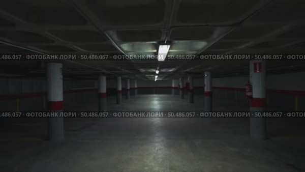 Shadowy underground parking garage with flickering fluorescent lights illuminating grey concrete columns, generating mysterious industrial ambiance through architectural perspective. Стоковое видео, видеограф Данил Руденко / Фотобанк Лори