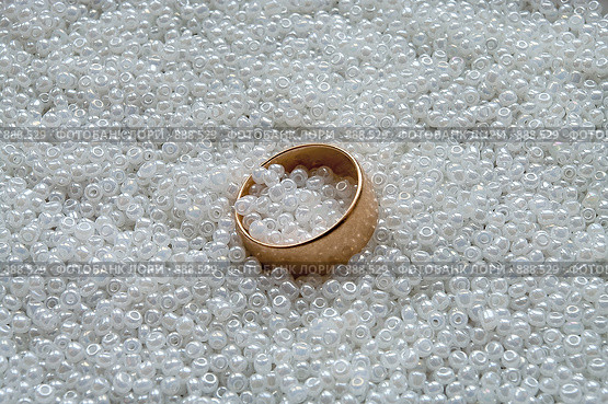 Широкое обручальное золотое кольцо лежит на белом бисере. Стоковое фото, фотограф Кекяляйнен Андрей / Фотобанк Лори