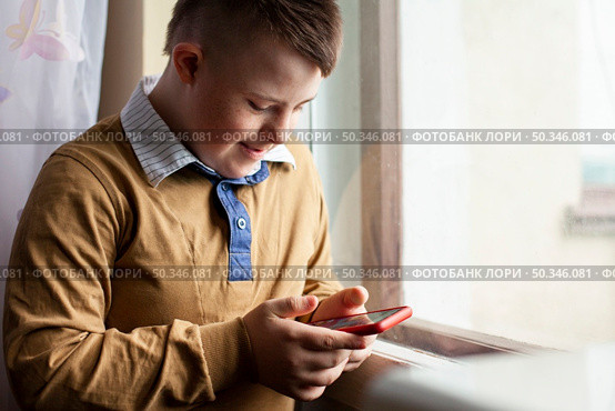 side view boy with down syndrome holding smartphone. Стоковое фото, агентство Ingram Publishing / Фотобанк Лори