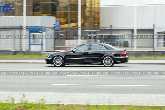 Side view rolling shot in black color sedan car in motion. Mercedes E-Class (W211) driving along the street in city with blurred background. Редакционное фото, фотограф Константин Григорьев / Фотобанк Лори