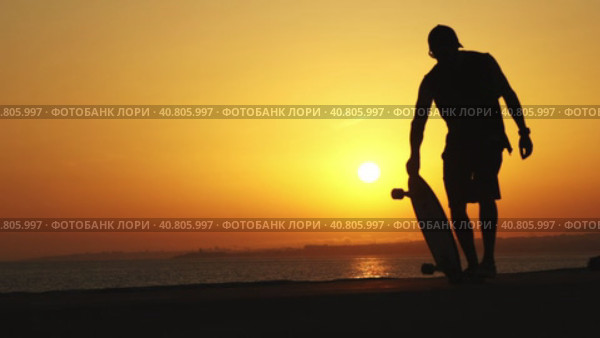 Silhouette of a man near the ocean with a longboard at bright orange sunset. Стоковое видео, видеограф Константин Шишкин / Фотобанк Лори