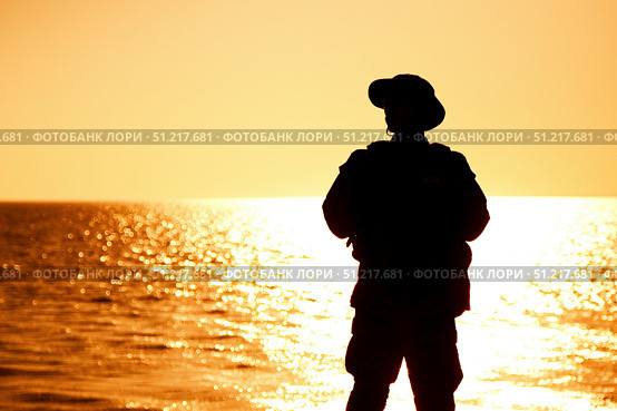 Silhouette of a soldier in boonie hat standing on the shoreline at sunset. Oleg Zabielin / Stocktrek Images/TASS. Стоковое фото, агентство ТАСС / Фотобанк Лори
