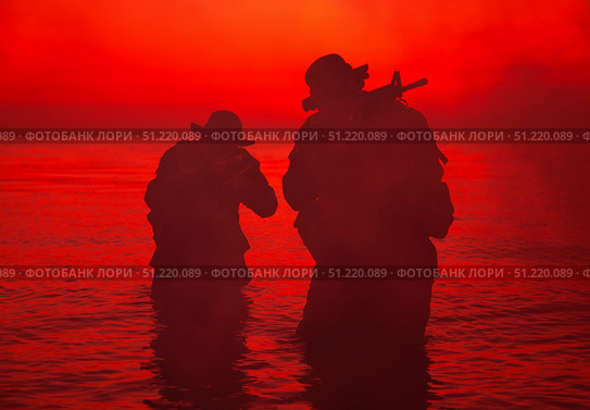 Silhouette of two soldiers wading the shoreline, sneaking in the darkness with assault rifles drawn. Oleg Zabielin / Stocktrek Images/TASS. Стоковое фото, агентство ТАСС / Фотобанк Лори