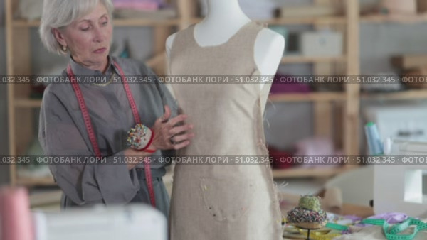 Skillful old tailoress trying prepared dress on mannequin in tailor shop. Стоковое видео, видеограф Яков Филимонов / Фотобанк Лори