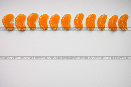 Slice sections of tangerine served on one line over the white background. Top view, copy space. Стоковое фото, фотограф Зарифа Арсланова / Фотобанк Лори