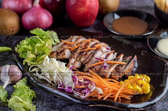Sliced ??pork steak with bread, carrots, cauliflower, lettuce and corn on a black plate on a cement floor. Стоковое фото, агентство Ingram Publishing / Фотобанк Лори