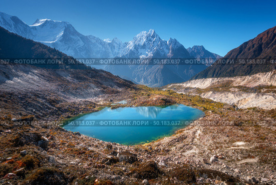 Small lake with blue water and sky reflection against beautiful snow covered mountains at sunny day in autumn. Landscape with lake, snowy rocks, hills, stones at sunrise. Himalayan mountains in Nepal. Стоковое фото, агентство Ingram Publishing / Фотобанк Лори