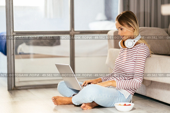 Smiling young woman with headphones and laptop on the sofa at home.. Smiling young woman with headphones and laptop on the sofa. Стоковое фото, агентство Ingram Publishing / Фотобанк Лори
