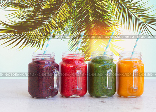 Smoothy drinks in glass jars on white table under plam tree. Fresh smoothy drink. Стоковое фото, агентство Ingram Publishing / Фотобанк Лори