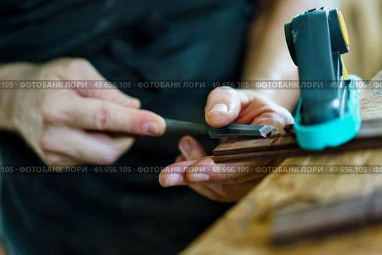 Soft focus of unrecognizable craftsman carving part for Spanish flamenco guitar on workbench during work in luthier workshop. Unrecognizable luthier crafting guitar part. Стоковое фото, агентство Ingram Publishing / Фотобанк Лори
