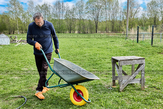 Solid polyurethane wheel recently installed is being inspected as gardener pushes garden wheelbarrow forward while slightly tilting to monitor new wheel performance. Стоковое фото, фотограф Владимир Григорьев / Фотобанк Лори