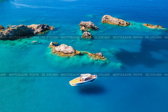 Speed boat on blue sea at sunrise in summer. Aerial view of motorboat on sea bay, rocks in clear azure water. Tropical landscape with yacht, stones. Top view from drone. Travel in Oludeniz, Turkey. Стоковое фото, агентство Ingram Publishing / Фотобанк Лори