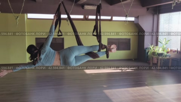 Спортивная женщина практикует йогу в гамаке, выполняет упражнение Васиштхасана, позу боковой планки, тренируется в спортивной одежде в студии. Стоковое видео, видеограф Сергей Чайко / Фотобанк Лори