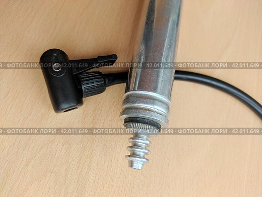 Sports tools: old aluminum hand pump with an attached ball's needle adapter, placed above the black hose. Compact metal pump with tiny scratches on its surfaces and a plastic adapter for bike' nipples. Стоковое фото, фотограф Анатолий Власов / Фотобанк Лори