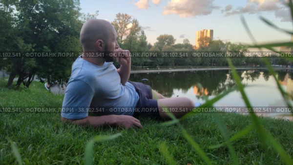 Спортсмен отдыхает на лоне природы после тренировки. Молодой кавказский мужчина лежит на траве возле озера или пруда в городском парке. Парень наслаждается прекрасным пейзажем. Летний вечер и закат. Athlete is resting in the lap of nature after training. Young caucasian man is lying on the grass near a lake or pond in a city park. Guy is enjoying the beautiful scenery. Summer evening and sunset. Стоковое видео, видеограф Ирина / Фотобанк Лори
