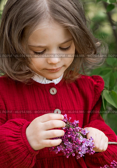 Spring blooming. Portrait of a beautiful 5-year-old little girl in a red dress in a lilac garden in nature. Childhood. Стоковое фото, фотограф Photojuli / Фотобанк Лори