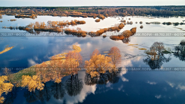 Spring flood rural landscape. Trees, meadow, bushes, fields, country road under High Water inundation. Sky and clouds reflection in evening light. Freshet Overflow aerial view. Floodplain area. Стоковое фото, агентство Ingram Publishing / Фотобанк Лори