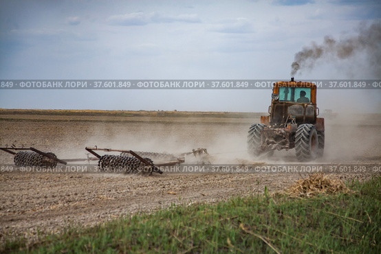 Spring sowing season. Tractor cultivated field soil with harrow. Стоковое фото, фотограф Alexey Rezvykh / Фотобанк Лори