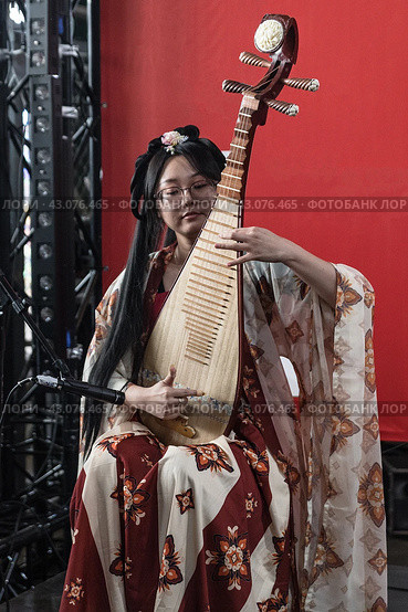 St. Petersburg, Russia-February 3, 2024: A young Chinese woman in a traditional costume plays a Chinese musical instrument called pipa. Редакционное фото, фотограф Регина Ерофеева / Фотобанк Лори