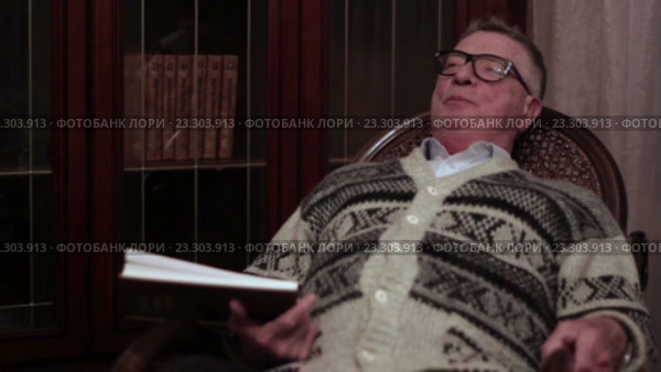 Старик в очках читает книгу вслух в кресле-качалке возле книжного шкафа. Стоковое видео, видеограф Video Kot / Фотобанк Лори