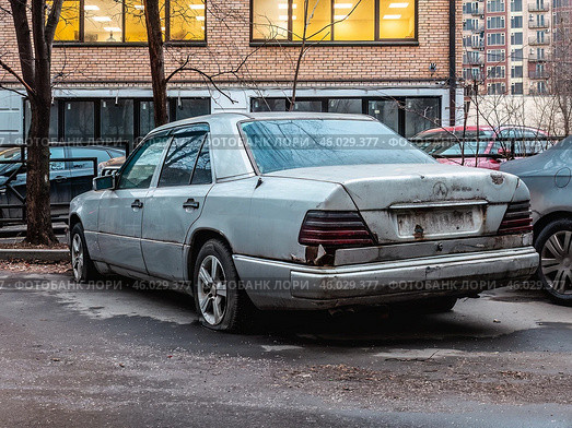 Старый брошенный автомобиль Mercedes W124 стоит во дворе дома. Неисправный сломанный автохлам. Редакционное фото, фотограф Константин Григорьев / Фотобанк Лори