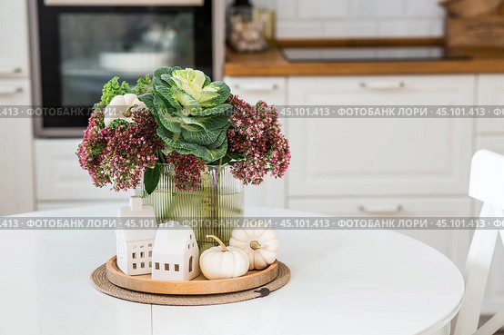 Still-life. A bouquet of decorative cabbage in a vase, pumpkins and white houses on the table in the interior of a home kitchen. A cozy autumn concept. Стоковое фото, фотограф Photojuli / Фотобанк Лори