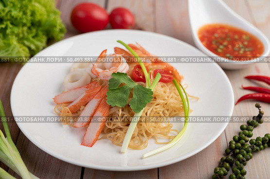 Stir-fried instant noodle with prawn and crab stick along with tomatoes and peppers in a white plate on a wooden floor. Стоковое фото, агентство Ingram Publishing / Фотобанк Лори